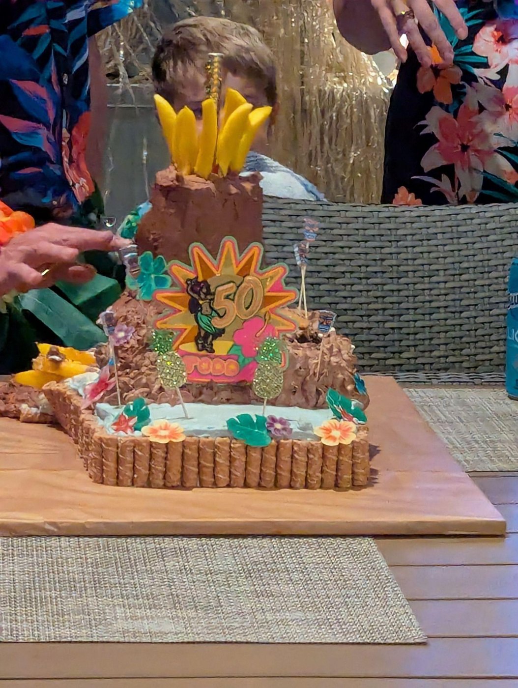 A volcano cake topped with a layered 50th birthday Luau cake topper and pineapple picks